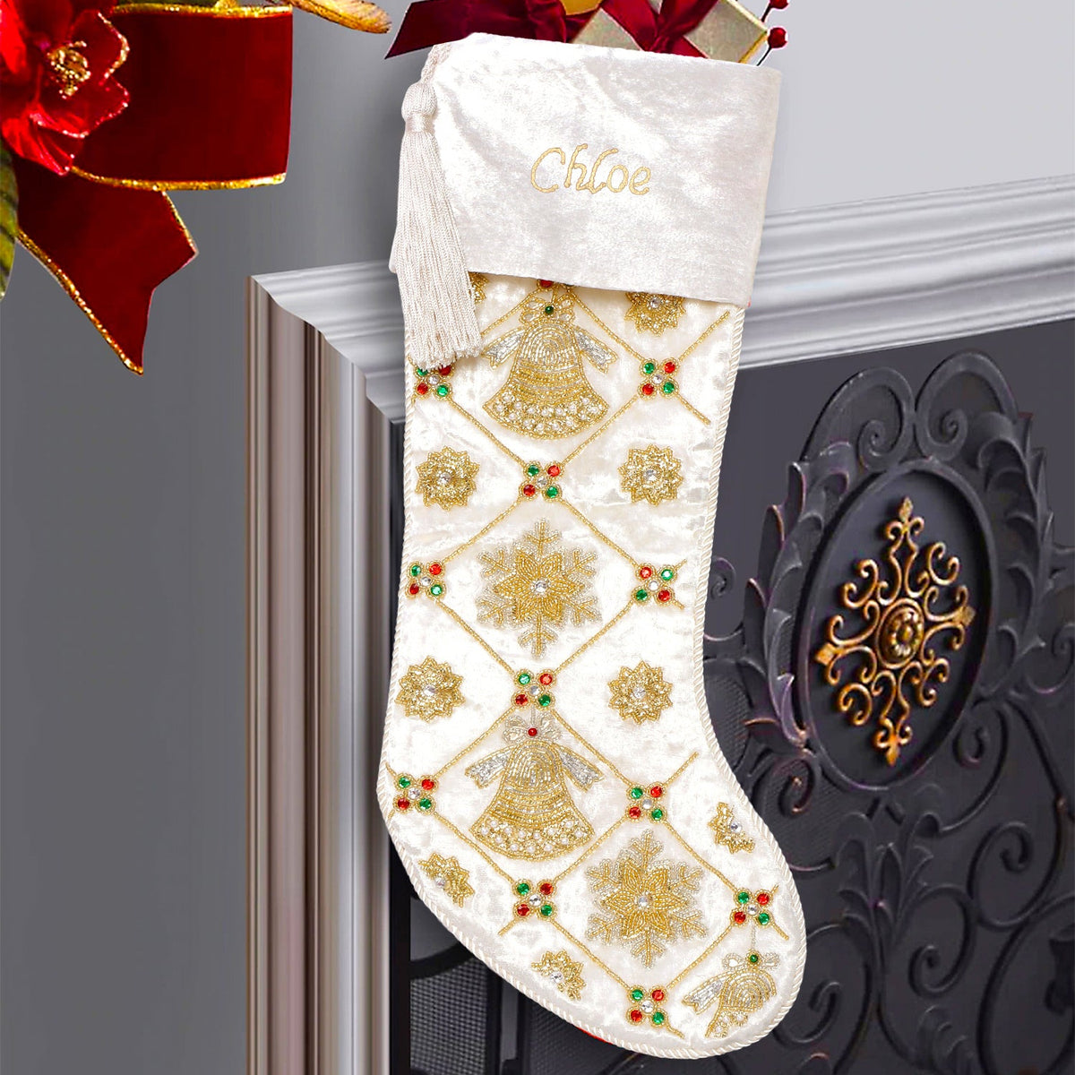A white velvet Christmas stocking with gold and silver snowflake patterns and embroidered details, hanging on a fireplace mantle.